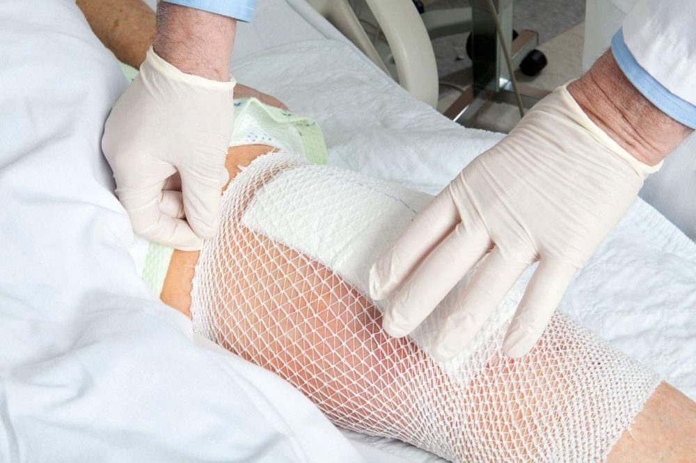A clinician in gloves dressing a wounded leg